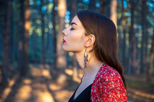 Profile view of beautiful young woman with eyes closed enjoying the sound of the woods.