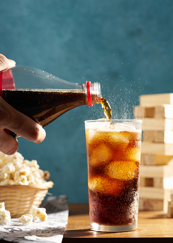hand pouring cola into a glass on wooden table with popcorn