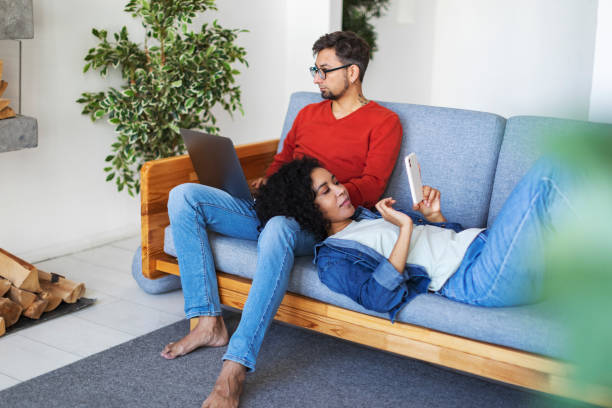 multiracial couple using laptop and mobile at home for work and leisure - multi ethnic group concentration mobile phone using laptop imagens e fotografias de stock