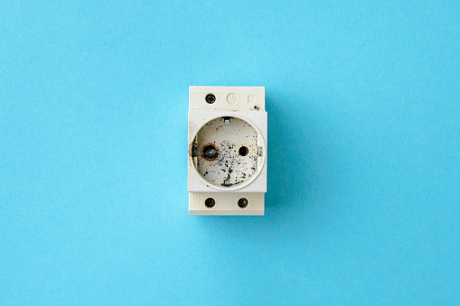 Broken din socket, electrical short circuit. The concept of electrical safety. Blue background, flat lay, close up