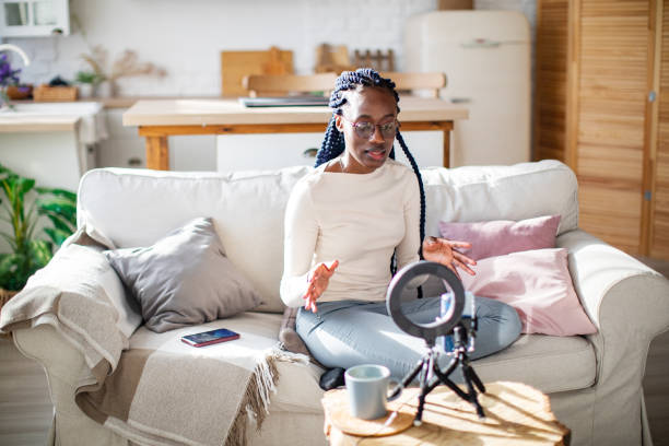 istock Young African woman streaming from home using mobile and ring lamp 1421368570