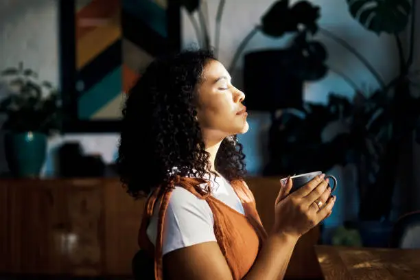 Photo of Relax, peace and coffee with a woman drinking a drink of caffeine and meditating in her home with her eyes closed. Mental health, wellness and zen with a young female enjoying calm, quiet tranquility