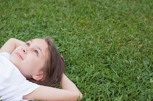 A happy little girl is lying on the green grass. A smiling child is resting, lying on the grass. The concept of a carefree childhood, a long-awaited summer, summer holidays