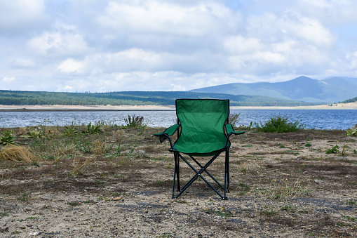 Empty camping chair at the lakeside with mountain and sky background, folding outdoor chair