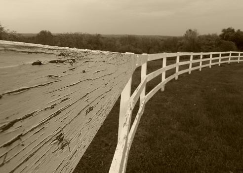 Sepia photo of a weathered white fence in the country.
