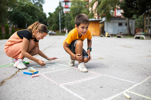 Cute tweenagers are drawing a hopscotch diagram in the schoolyard