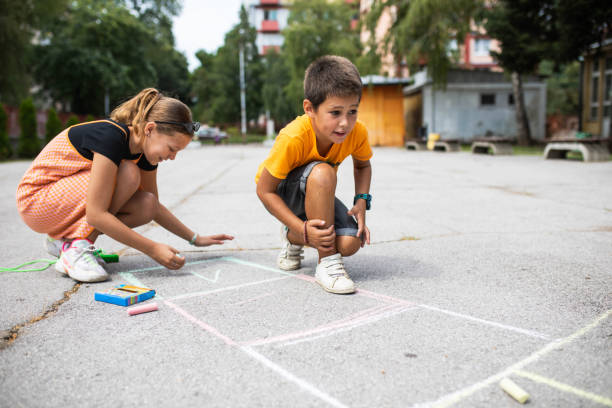 School kids writing numbers in hopscotch boxes in the schoolyard stock photo