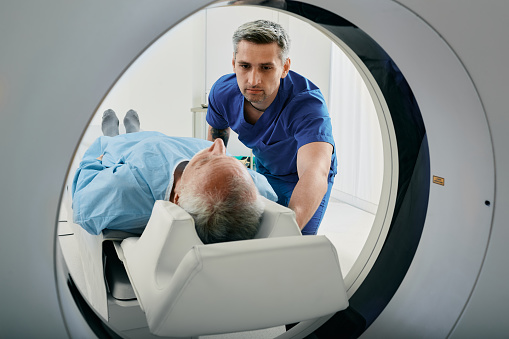 Hombre mayor que entra en un escáner de TC. Tecnólogo de tomografía computarizada que pasa por alto al paciente en el escáner de tomografía computarizada durante la preparación para el procedimiento photo