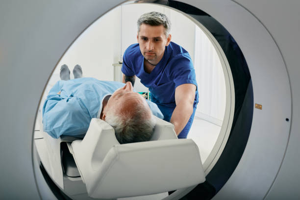 senior man going into ct scanner. ct scan technologist overlooking patient in computed tomography scanner during preparation for procedure - medische scan stockfoto's en -beelden