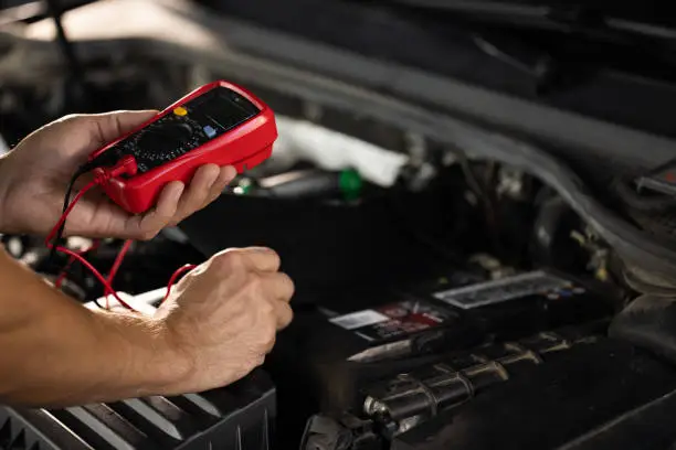 Photo of Check battery voltage with electric multimeter. Man using multimeter to measure the voltage of the batteries. Mechanic doing car inspection, he is testing car battery with tester