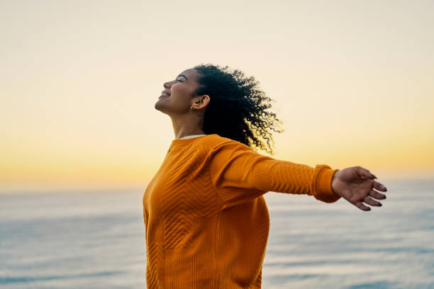 Freedom, liberty and happy black woman celebrating being free at sunset at beach, positive and excited. Young female enjoying beach getaway and spiritual power while standing and breathing fresh air stock photo