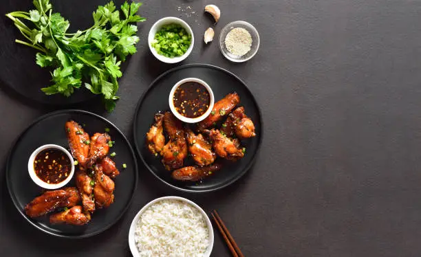 Sticky honey-soy chicken wings on plate over dark stone background with copy space. Top view, flat lay