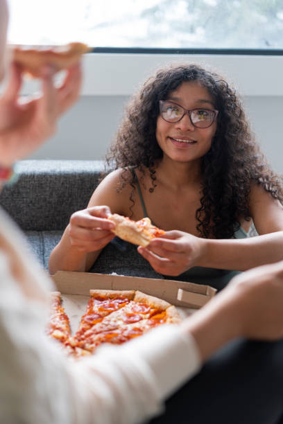 dwaj latynoscy przyjaciele spędzają razem czas w salonie swojego domu, jedząc kawałek pizzy - pizza pizzeria friendship people zdjęcia i obrazy z banku zdjęć