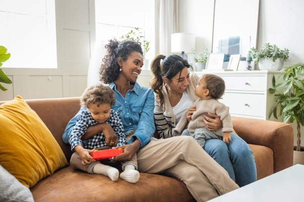 Female gay couple with kids at home Young mothers playing with kids in living room. lesbian stock pictures, royalty-free photos & images