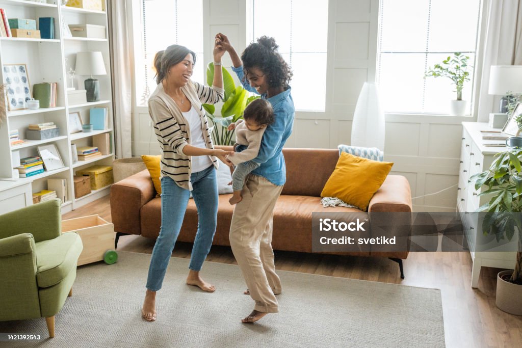 Female gay couple with baby at home Young mothers playing and dancing with baby girl in living room. Dancing Stock Photo