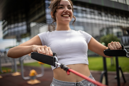 A young teenage female athlete uses a resistance band while exercising outdoors at a gym near her college