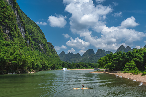 Yangshuo, China - August 2019 : Old fisherman paddling on a small narrow wooden boat among stunning karst mountain scenery on the magnificent Li river