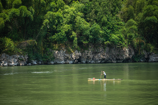 Yangshuo, China - August 2019 : Old fisherman paddling on a small narrow wooden boat among stunning karst mountain scenery on the magnificent Li river