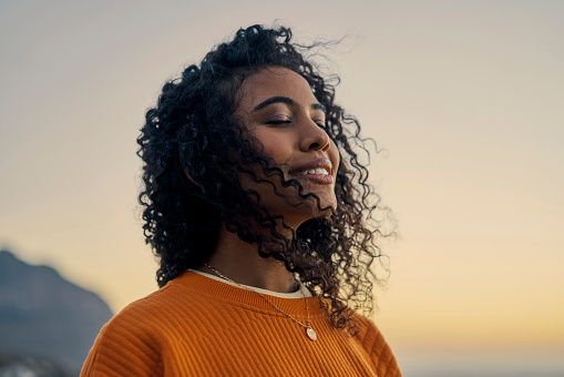 Happy woman in nature, sunset sky peace and smile breathing co2. Wellness beauty, clear outdoor sky and\nfresh wave of calm. Eyes closed, asthma treatment air and girl with curly hair relaxed face.