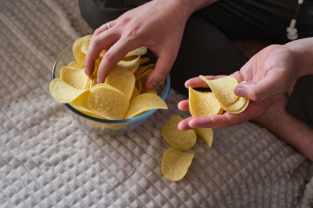 istock A man eats crispy potato chips from a transparent bowl on the couch. Quick snack. Calories and diet 1421402671