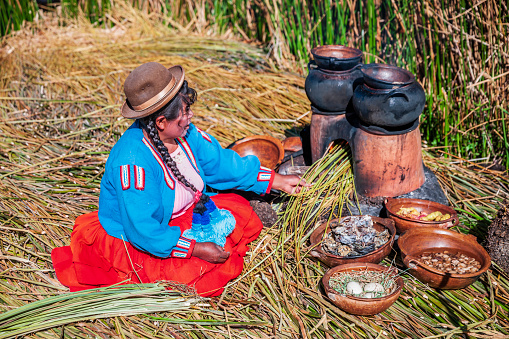 Peruvian woman preparing a meal on Uros floating island, Lake Tititcaca. Uros are a pre-Incan people that live on forty-two self-fashioned floating island in Lake Titicaca Puno, Peru and Bolivia. They form three main groups: Uru-Chipayas, Uru-Muratos  and the Uru-Iruitos. The latter are still located on the Bolivian side of Lake Titicaca and Desaguadero River. The Uros use bundles of dried totora reeds to make reed boats (balsas mats), and to make the islands themselves. The Uros islands at 3810 meters above sea level are just five kilometers west from Puno port.
