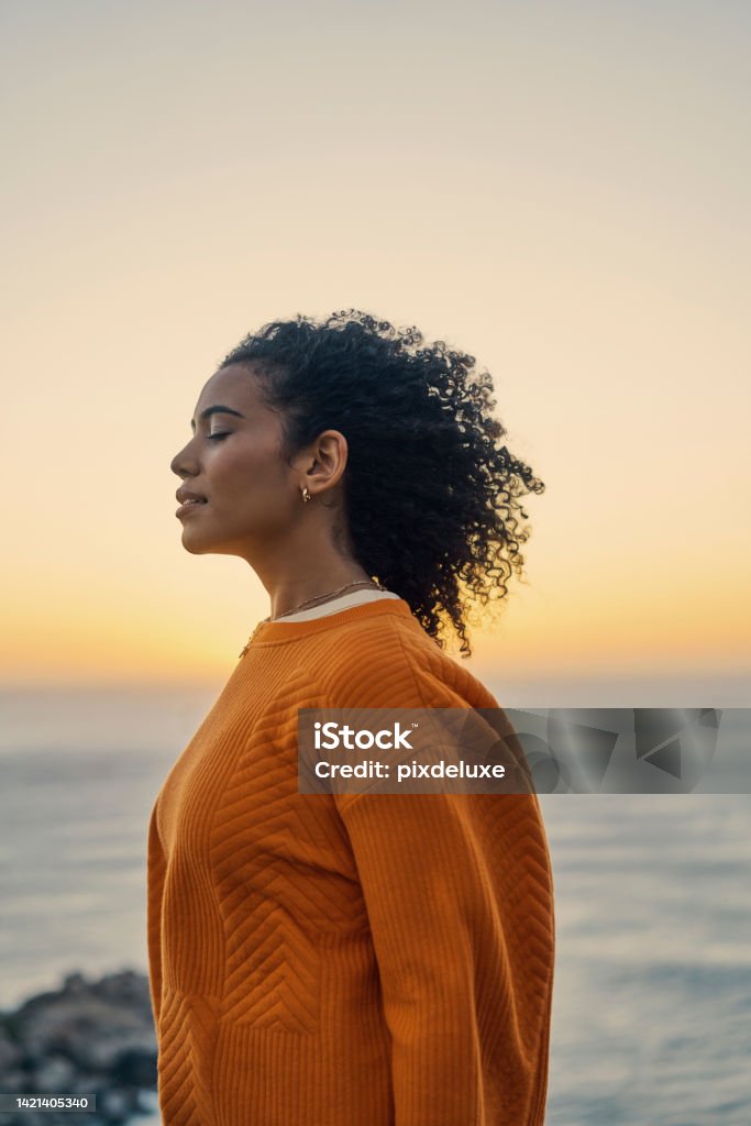 Relax, zen and freedom mindset of a woman at the ocean water, beach and sea in nature at sunset. Calm and positive energy of a young Moroccan female enjoying the sound of content waves at evening Zen-like Stock Photo