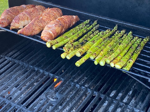 Image of bacon wrapped chicken and fresh asparagus on the top rack of a bbq being grilled for dinner