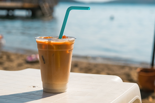 Ice latte coffee with a straw on the table. Man drinking coffee. Plastic cup of coffee on the beach.