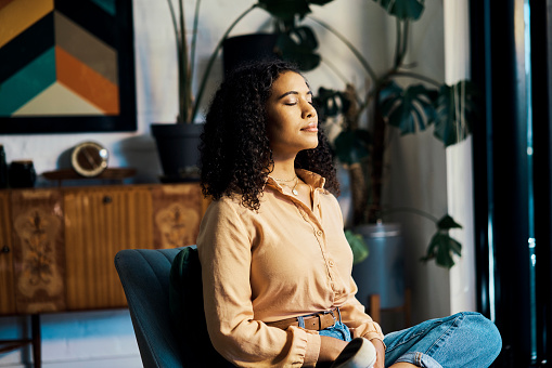Meditation, calm and african woman sitting alone and feeling mindful and free while doing a breathing exercise for mental health and wellness. Young zen female sitting at home to relax and meditate