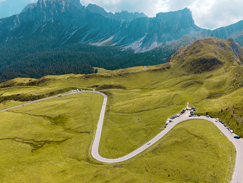Dolomite Alps in Italy. View of mountains and slopes covered with greenery and forest, low clouds, road with cars