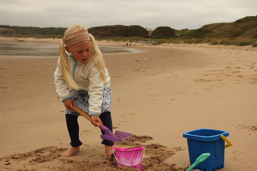 Little girl digging on beach with bucket and spade on an overcast day