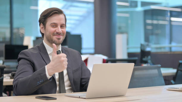 istock Businessman Showing Thumbs Up Sign While using Laptop in Office 1421432030