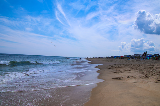 A wide angle view of the beach with umbrellas set up on the right side and waves coming on the left side. The lifeguard is also visible in the distance with interesting clouds in the sky.