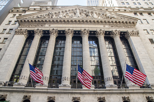 Facade of New York Stock Exchange with American flags during summer day