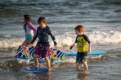 Ocean City, USA - September 3, 2022. Three children walking in water with their bodyboards at Ocean City, New Jersey, USA