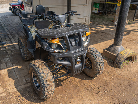 A front view of an All-Terrain Vehicle, or ATV, with dominant black color and four off road tires, idle for rent on an amusement park.