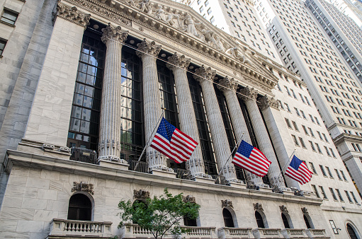 Wall Street sign with american flags and New York Stock Exchange in Manhattan, New York City, USA.