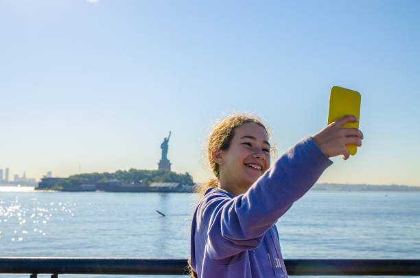 Teenage girl taking selfie with Statue of Liberty from Liberty State Park Teenage girl taking selfie with  Statue of Liberty from Liberty State Park in New Jersey on summer day mobile sculpture stock pictures, royalty-free photos & images