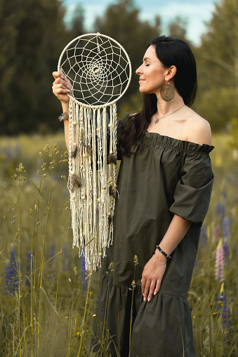 An attractive woman in a summer field with a dream catcher. Vertical photo.