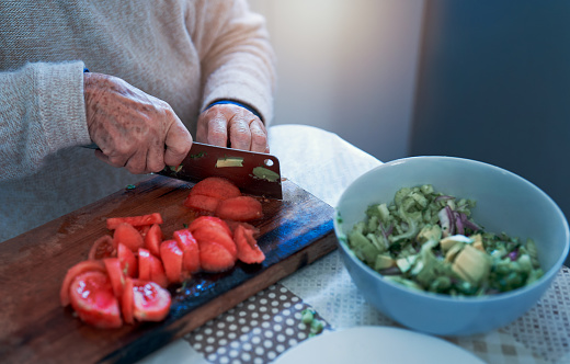 view of senior woman's hands cutting tomatoes on a wooden board in the kitchen