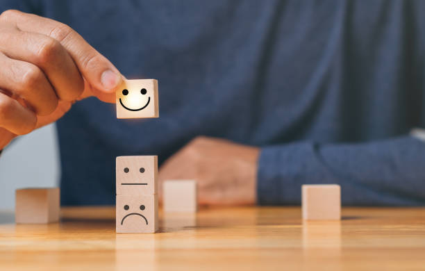 istock Top Smile Satisfaction. Best excellent business services rating customer experience. Satisfaction survey concept. Hand of a businessman chooses a smiley face on wood block cube. 1421453602