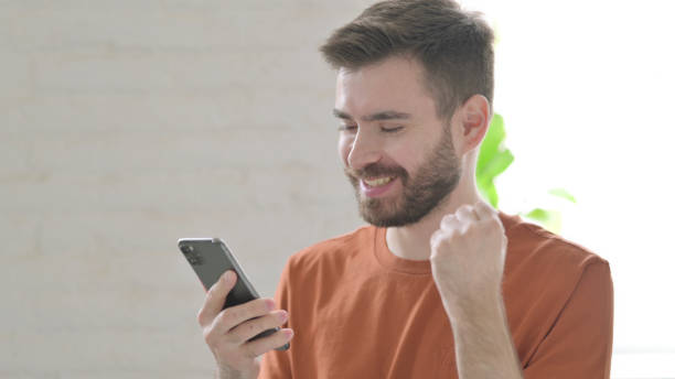 istock Young Man Celebrating Success on Smartphone 1421454099