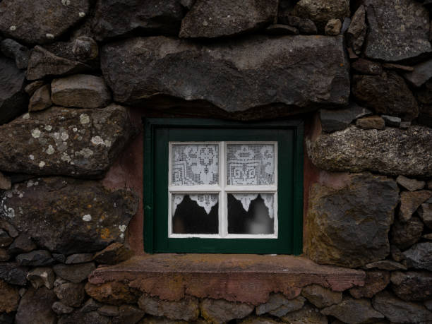 Detail of a wooden window, with a crocheted curtain, in one of the houses in the historic Aldeia da Cuada.\nFlores Island, Portugal.