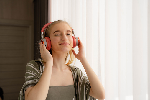 Relaxed young Asian woman enjoying music over headphones from smartphone at home.