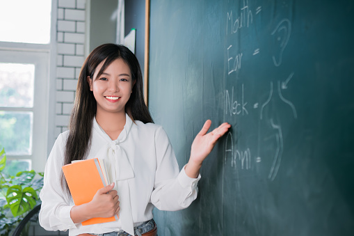 Portrait attractive of smiling Asian Teacher woman teaching student in classroom, Female teacher writing on blackboard, High school and back to school concept.