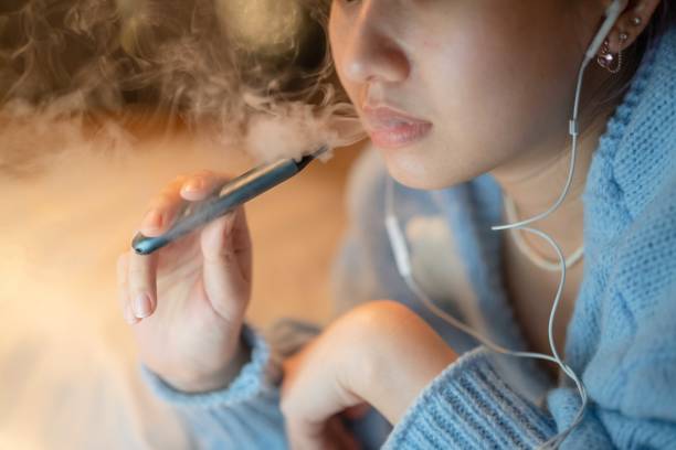 Stressful woman smoking electronic cigarette for relax. Young woman vaping an electronic cigarette for relax while working at night electronic cigarette stock pictures, royalty-free photos & images