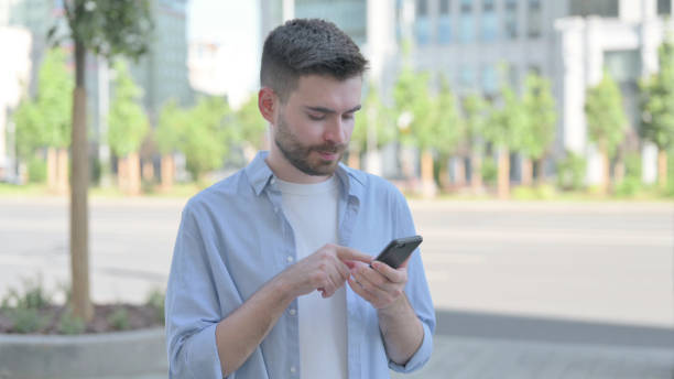 istock Young Man Browsing Internet on Smartphone Outdoor 1421479586