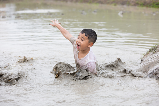 Happy little boy child playing in large wet mud and dirt on summer day
