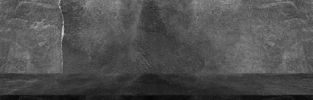 istock Dark black wide horizontal decorative cement wall room background with light and shadow abstract wallpaper background 1421484059