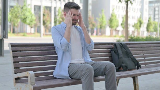 istock Young Man with Headache Sitting on Bench 1421485931